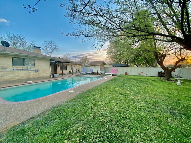 pool at dusk featuring a yard, a fenced in pool, and a fenced backyard