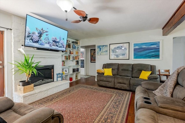 living area featuring a glass covered fireplace, wood finished floors, built in features, and a ceiling fan