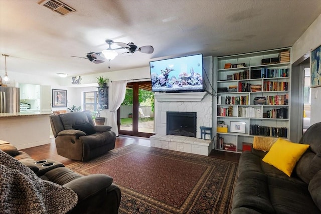 living room with a stone fireplace, a ceiling fan, wood finished floors, and visible vents