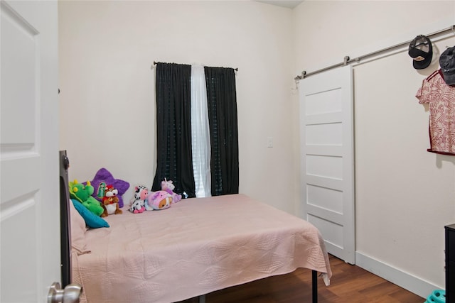 bedroom with baseboards, a barn door, and wood finished floors