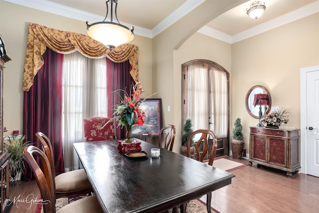 dining space with wood finished floors, crown molding, and arched walkways