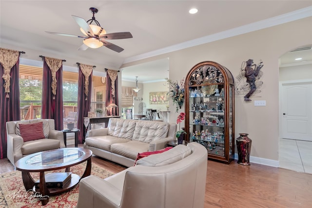 living area featuring light wood-type flooring, a ceiling fan, baseboards, ornamental molding, and arched walkways