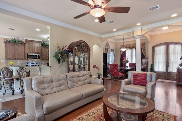 living area featuring arched walkways, visible vents, a ceiling fan, and ornate columns