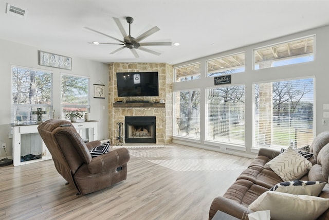 living area featuring wood finished floors, a stone fireplace, a healthy amount of sunlight, and ceiling fan