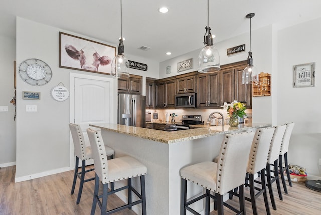 kitchen featuring dark brown cabinetry, light stone countertops, appliances with stainless steel finishes, a peninsula, and visible vents