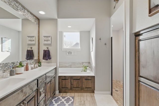 full bath with double vanity, a sink, wood finished floors, and a bath