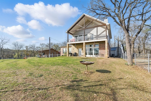 rear view of property featuring a balcony, fence, a chimney, brick siding, and a lawn