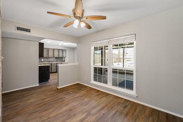 unfurnished living room featuring visible vents, baseboards, ceiling fan, and dark wood-style floors