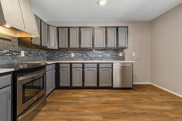 kitchen featuring gray cabinets, backsplash, custom range hood, light countertops, and stainless steel appliances