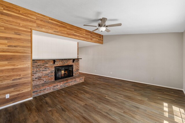 unfurnished living room featuring ceiling fan, a fireplace, wood walls, wood finished floors, and baseboards