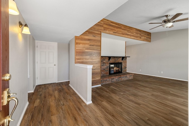 unfurnished living room featuring baseboards, a ceiling fan, wood walls, and wood finished floors