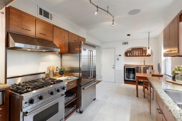 6814 Blackwood Dr, Dallas, TX 75231 - kitchen featuring under cabinet range hood, high quality appliances, beverage cooler, brown cabinetry, and light wood-style floors