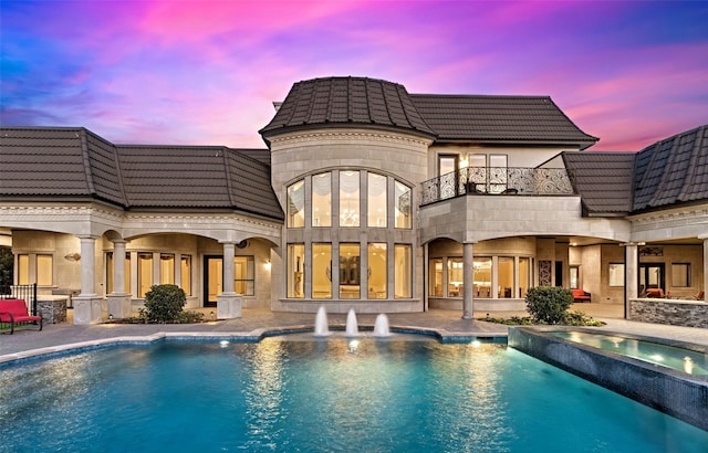 back of house featuring a tile roof, a balcony, a patio area, and a pool with connected hot tub