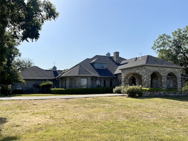 french country home with a chimney, brick siding, and a front yard