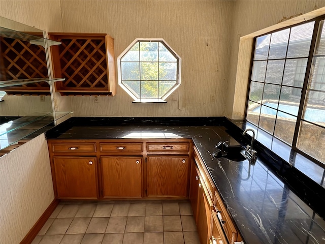 kitchen with a sink, wallpapered walls, light tile patterned floors, and brown cabinets
