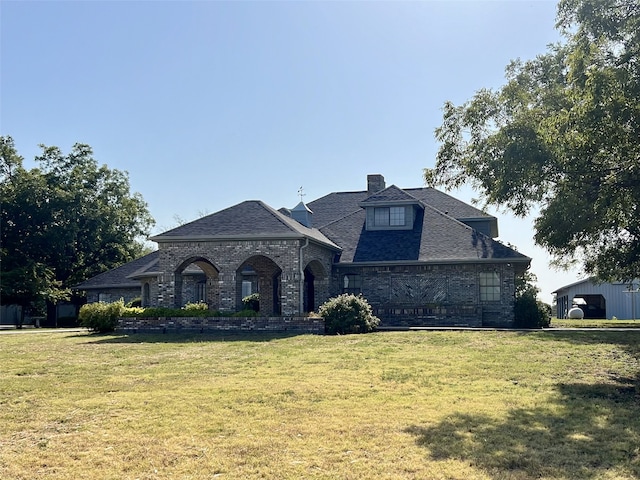 french provincial home with a chimney, a front yard, brick siding, and roof with shingles