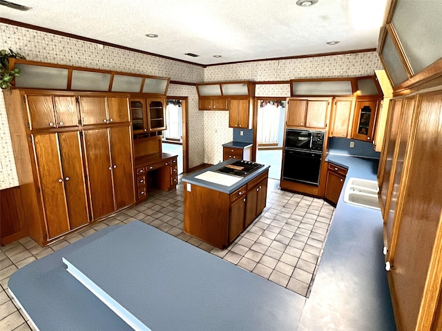 kitchen with a center island, a textured ceiling, wallpapered walls, black appliances, and brown cabinetry
