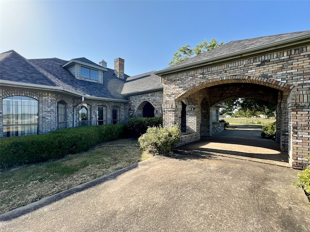 view of front of home with driveway, a chimney, and brick siding