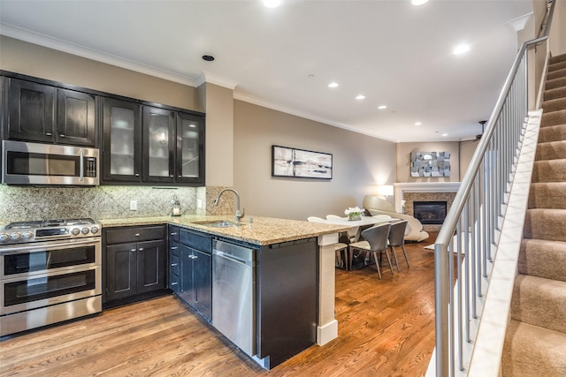 kitchen with a peninsula, appliances with stainless steel finishes, a sink, open floor plan, and light wood finished floors