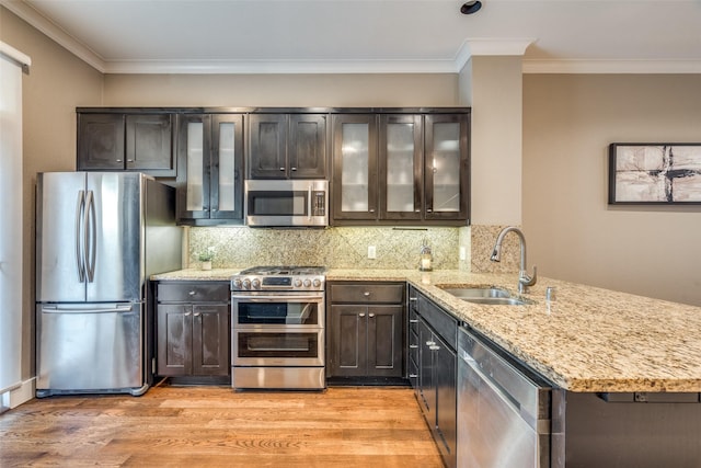 kitchen with a sink, a peninsula, stainless steel appliances, light wood-style flooring, and light stone counters
