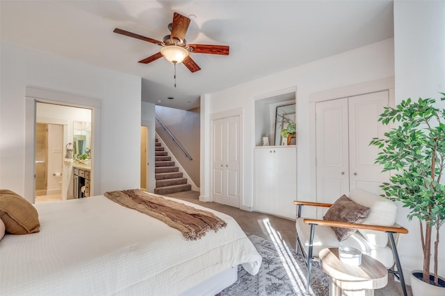 bedroom with ensuite bath, light colored carpet, two closets, and a ceiling fan