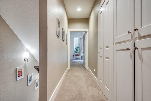 hall with light carpet, baseboards, and a textured wall