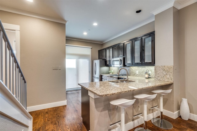 kitchen with a sink, appliances with stainless steel finishes, a breakfast bar, backsplash, and light stone counters