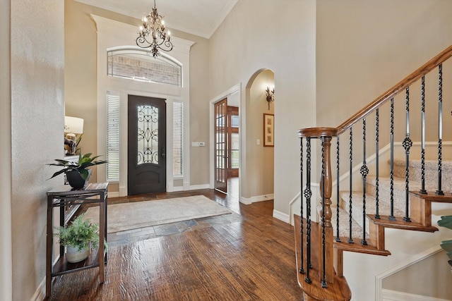 foyer entrance featuring arched walkways, wood finished floors, a chandelier, a towering ceiling, and baseboards