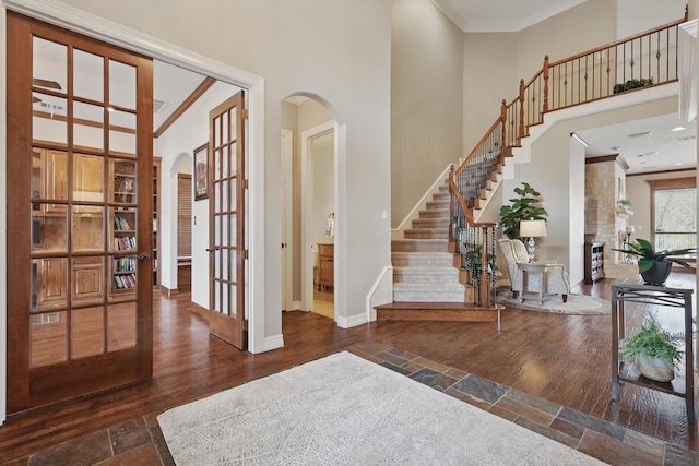 foyer entrance featuring arched walkways, a towering ceiling, baseboards, crown molding, and stairs