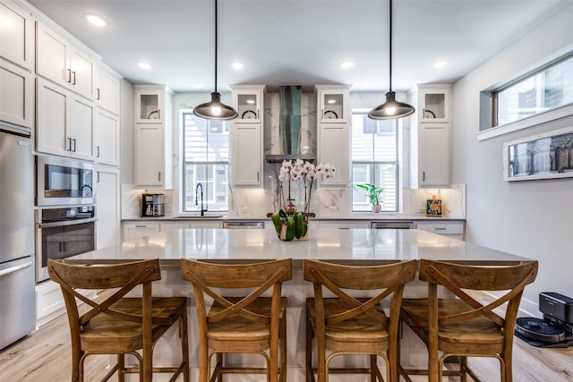 2716 Flowering Peach Ln, Dallas, TX 75212 - kitchen featuring appliances with stainless steel finishes, wall chimney range hood, decorative backsplash, glass insert cabinets, and light wood-style floors