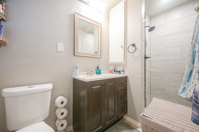 full bathroom with toilet, vanity, a textured wall, and tiled shower