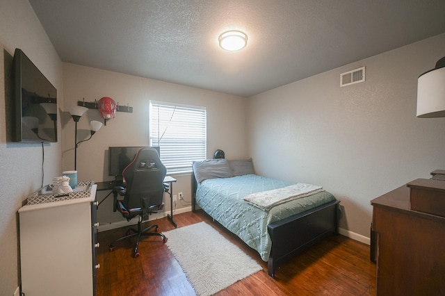 bedroom featuring wood finished floors, a textured ceiling, baseboards, and visible vents