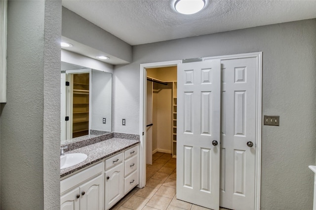 112 Woodcrest St, Weatherford, TX 76087 - bathroom featuring vanity, a spacious closet, a textured ceiling, tile patterned floors, and a textured wall