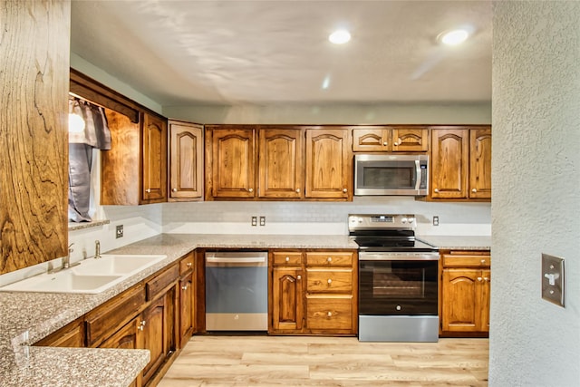 112 Woodcrest St, Weatherford, TX 76087 - kitchen featuring stainless steel appliances, brown cabinetry, a sink, light wood-style flooring, and a textured wall