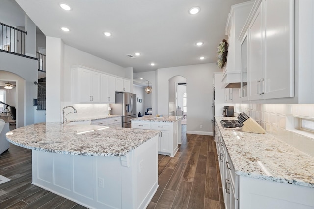 kitchen with wood finish floors, a kitchen island, arched walkways, and appliances with stainless steel finishes