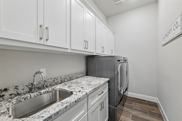laundry area featuring wood finish floors, baseboards, a sink, cabinet space, and washer and dryer
