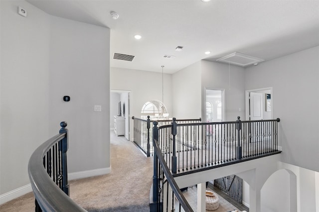 corridor with an upstairs landing, visible vents, baseboards, attic access, and light carpet