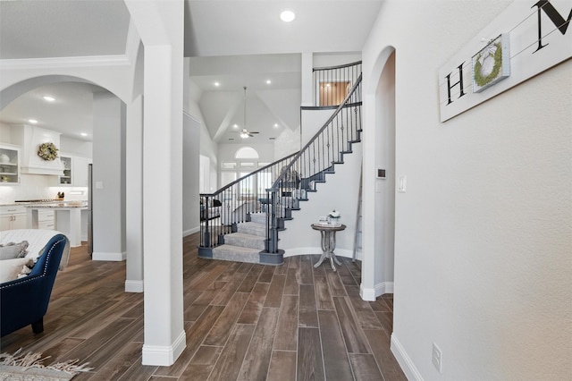 foyer entrance with dark wood-type flooring, arched walkways, baseboards, and stairway