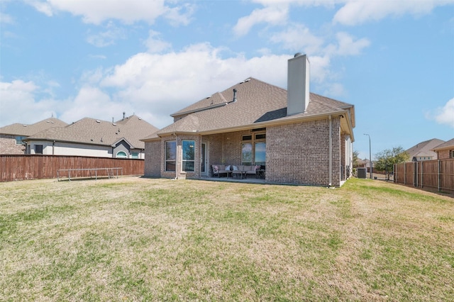 rear view of property featuring a trampoline, brick siding, and a yard