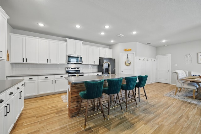 6028 Bowie Ct, Providence Village, TX 76227 - kitchen featuring appliances with stainless steel finishes, a kitchen breakfast bar, decorative backsplash, light wood-style flooring, and a kitchen island with sink