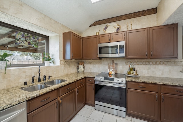 kitchen featuring light tile patterned floors, a sink, vaulted ceiling, tasteful backsplash, and appliances with stainless steel finishes
