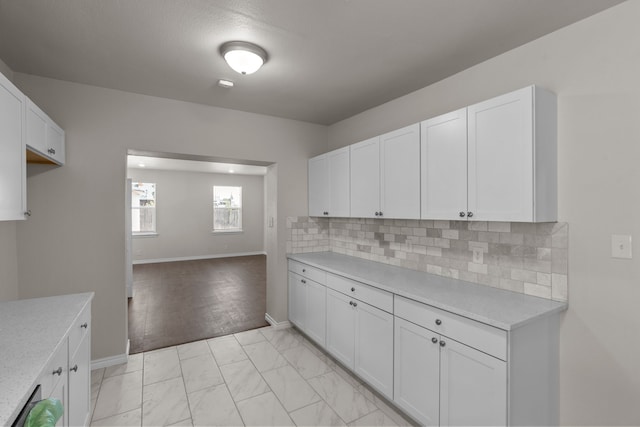 4601 Virginia Ln, Fort Worth, TX 76103 - kitchen with backsplash, white cabinets, baseboards, light marble finish floors, and light stone countertops