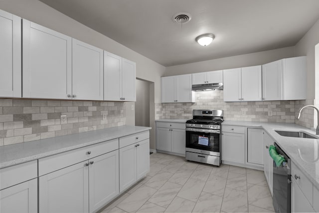4601 Virginia Ln, Fort Worth, TX 76103 - kitchen with stainless steel appliances, under cabinet range hood, a sink, light marble finish floors, and white cabinets