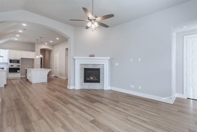 1916 Pelham Dr, Aubrey, TX 76227 - unfurnished living room featuring lofted ceiling, a ceiling fan, arched walkways, light wood-style flooring, and a fireplace