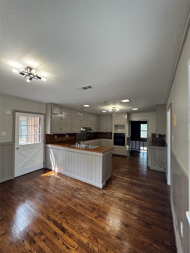 kitchen with dark wood-style flooring, a textured ceiling, a peninsula, and oven