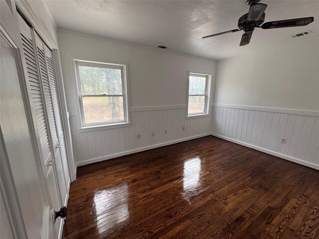 unfurnished bedroom with visible vents, a ceiling fan, wainscoting, and wood finished floors