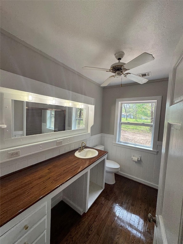 bathroom featuring toilet, a textured ceiling, wood finished floors, and a wainscoted wall