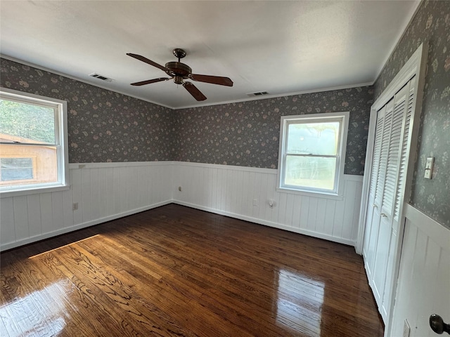 unfurnished bedroom with a closet, wainscoting, wood finished floors, and visible vents