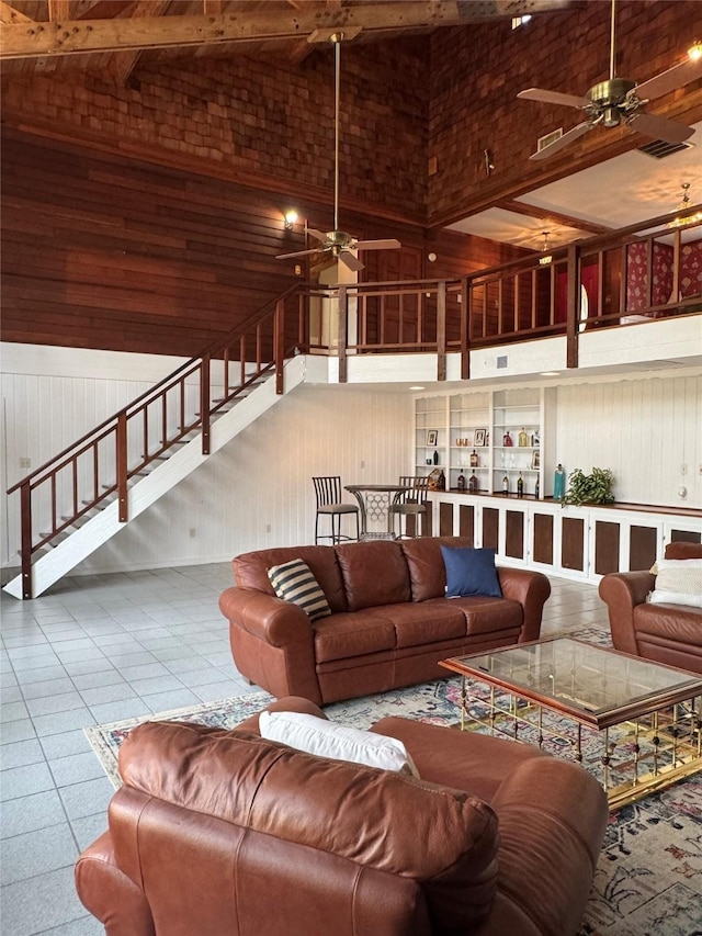 living area with high vaulted ceiling, tile patterned floors, a ceiling fan, beamed ceiling, and stairway