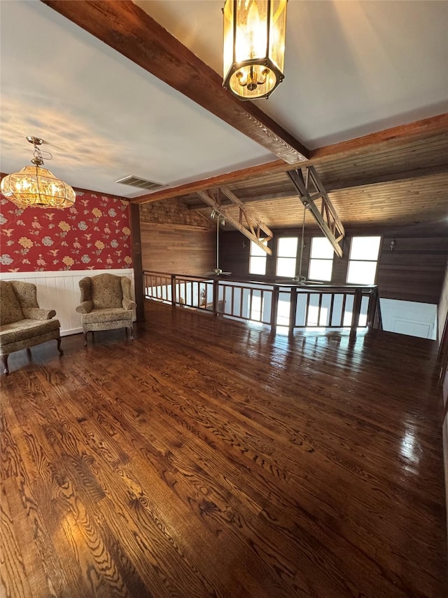 unfurnished room featuring beam ceiling, a wainscoted wall, wallpapered walls, wood finished floors, and visible vents
